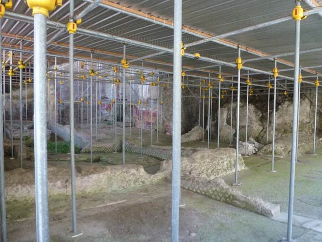 House of Dionysiac Reliefs, Herculaneum. June 2012.
Under the metal roof, at the side of the baths complex is part of a large residential building
Looking north-east from room (q), lower left.
On the extreme left, centre of photo, is the fountain in room (p), at the rear of it is room (l3).
In front of it, and between it and room (q), is the biclinium room (n).
In the centre of the photo, with painted walls, is room (m), with a doorway leading south into room (o).
On the extreme right is another room (f2), with a doorway leading north into room (o).
At the side of room (o) are rooms (u), (t) and (v).
Photo courtesy of Michael Binns.